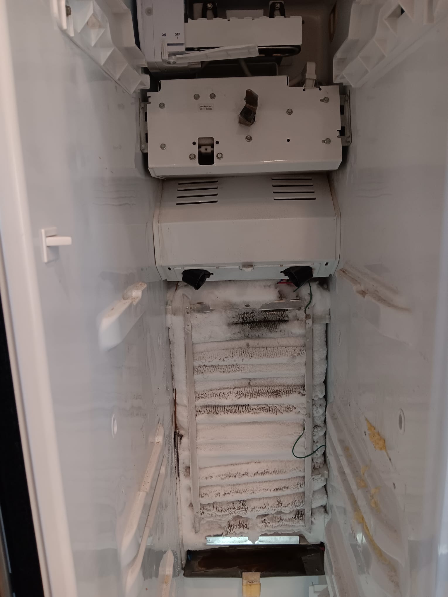 Heavy frost and ice buildup covering the evaporator coils inside a GE refrigerator's freezer compartment