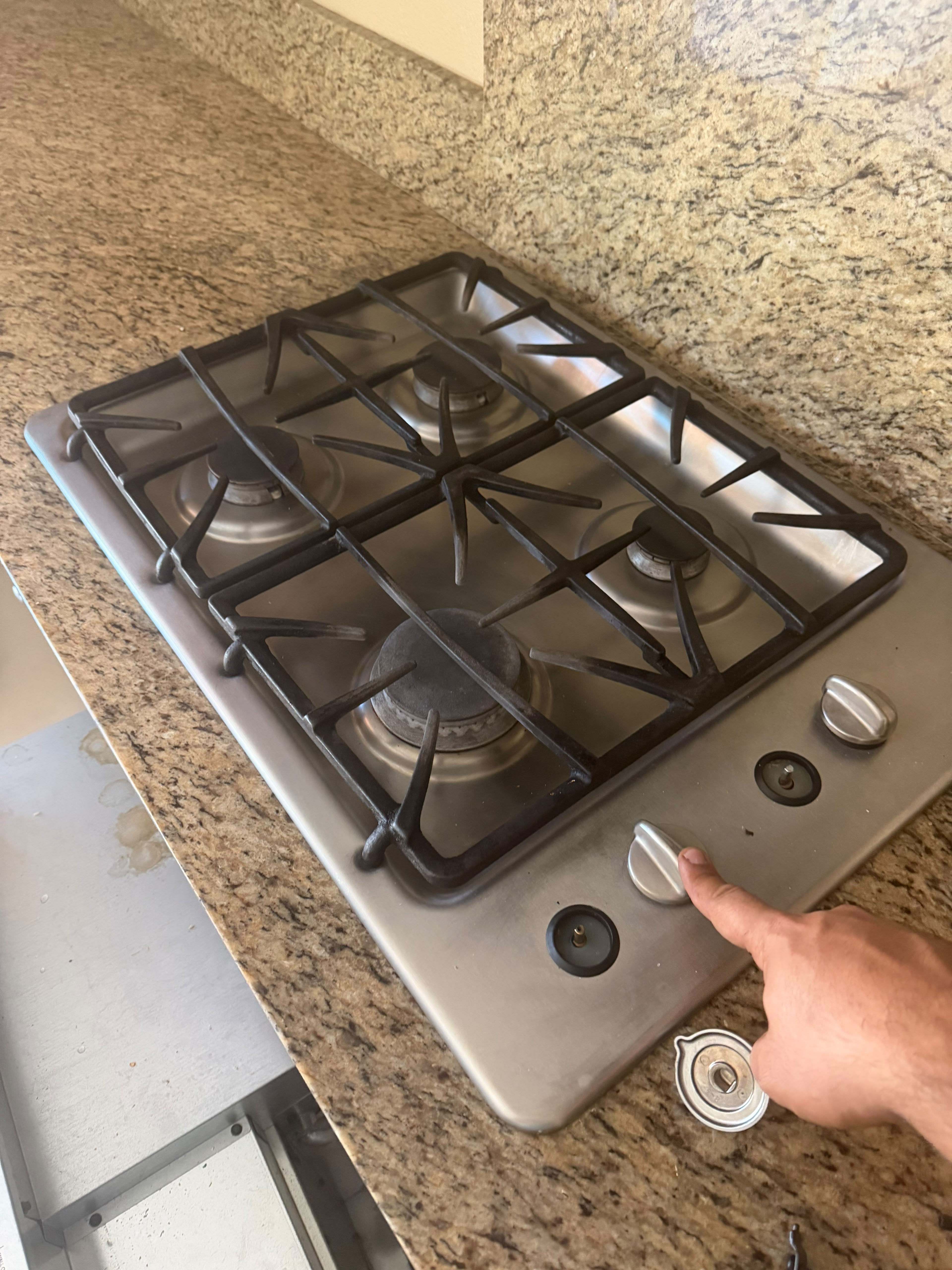 Technician pointing out the faulty burner gas valve on the GE cooktop with the knobs removed