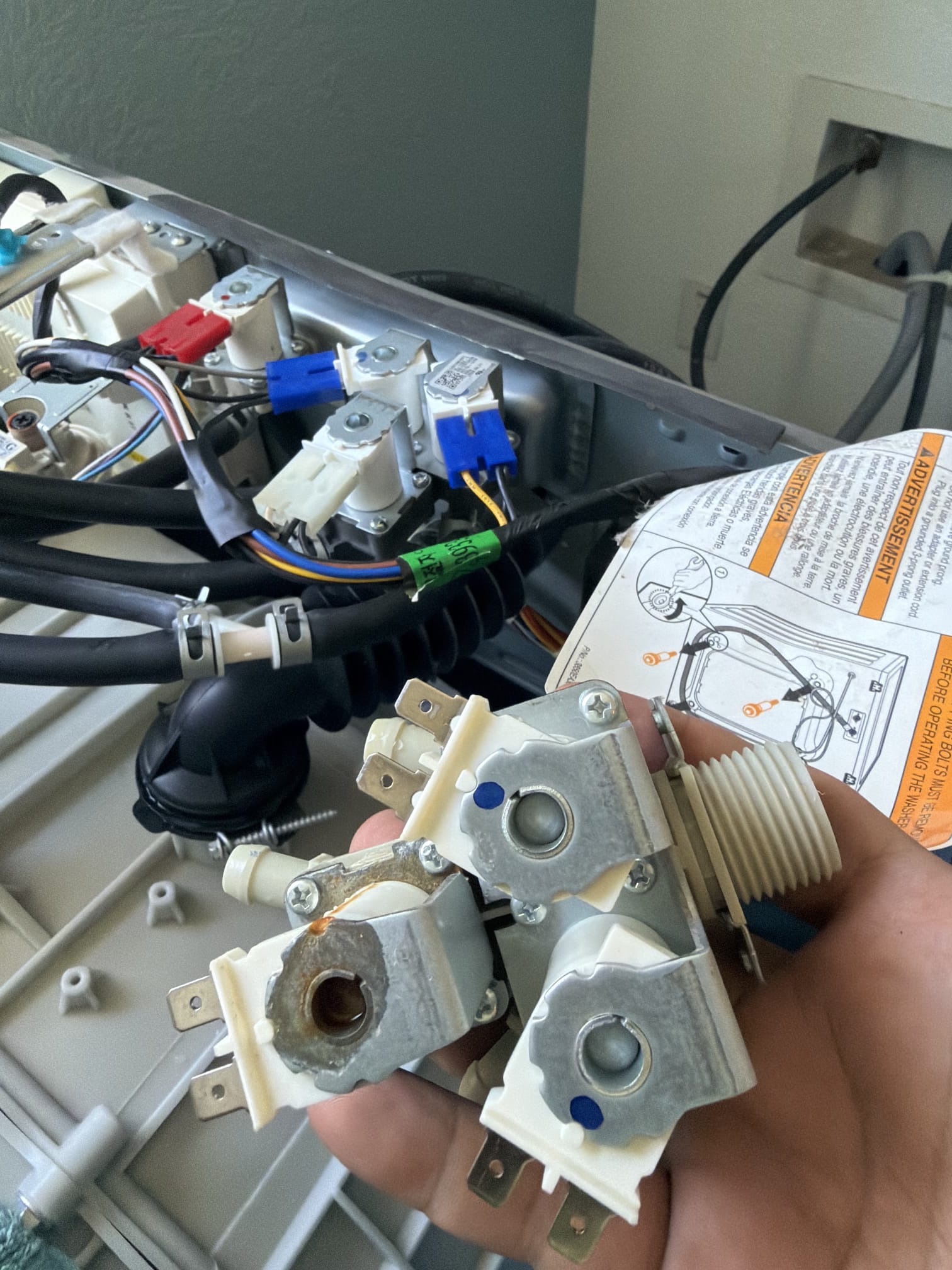 Corroded water inlet valve assembly removed from the Kenmore Elite washer, held next to the open top panel wiring